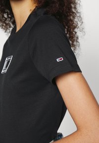 Černé bavlněné tričko s kulatým výstřihem, krátkými rukávy a malým logem na levém rukávu, na přední části s čtvercovým logem.