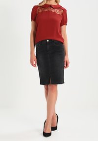 Blouse rouge avec détail en dentelle et col, associée à une jupe en denim noir ajustée avec une fente à l'avant. Des talons noirs complètent la tenue.