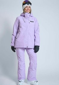 Lilla skijakke med justerbar hætte og frontlynlås, parret med matchende bukser. Sorte handsker og goggles tilføjer kontrast. Glat tekstur.