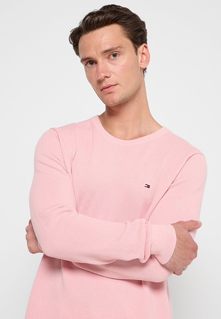 Rosa langärmliges Shirt aus strukturiertem Stoff, mit einem runden Ausschnitt und einem kleinen Logo auf der Brust. Der Schnitt ist lässig.