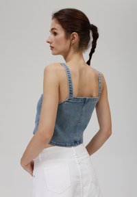 Denim vrhnji del z tankimi naramnicami, svetlo modre barve, z rahlo zbledelim videzom in oprijetim dizajnom. Ujemajoče visoke bele kratke hlače.