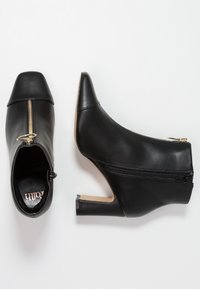 Botines de piel negra hasta el tobillo con punta afilada, cremallera interior y un detalle de metal dorado. Tacón de aguja y acabado suave.