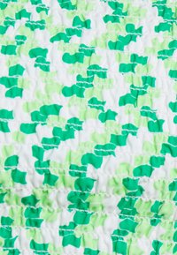 Tecido verde e branco com um padrão ondulado de pequenas formas abstratas. Texturizado e reunido com filas de costura por todo o tecido.