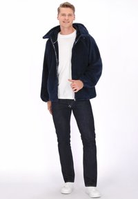 Granatowa kurtka polarowa z zamkiem z przodu, kapturem i bocznymi kieszeniami, zestawiona z ciemnymi dżinsami i białymi trampkami. Gładka faktura i przytulny design.