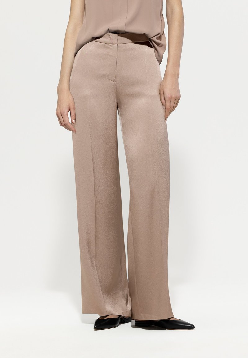 Light pink wide-leg trousers made of a smooth satin fabric, featuring a straight cut and subtle sheen, paired with black pointed shoes.