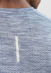 Ljusblå atletisk tröja med strukturerat mönster, rund halsringning och en vertikal vit accent på ryggen.