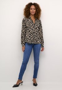 Blusa nera con stampa leopardata, maniche lunghe e colletto, abbinata a jeans skinny blu e mule con tacco neri. Tessuto liscio, frontale con bottoni.