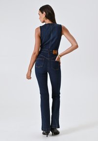 Denim jumpsuit met een aansluitende pasvorm, flare benen, donker denim en twee achterzakken; inclusief een leren merkpatch op de taille.