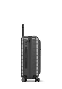Valise rigide grise avec des rainures horizontales, poignée rétractable, serrure TSA et quatre roues pour la mobilité. Compartiment à glissière sur le côté.