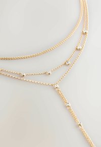 Colier auriu cu straturi, format din multiple lanțuri, având accente circulare mici de cristal distanțate uniform de-a lungul firelor, creând un design delicat.