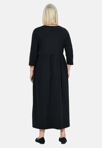 Černé dlouhé šaty s nabíraným pasem, splývavou sukní a hladkým povrchem. Pohled zezadu. Jednoduchý design, bez vzorů nebo akcentů.