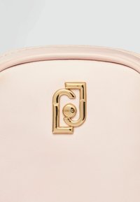 Handtasche aus hellrosa Stoff mit einem goldfarbenen Logo-Detail, glatter Textur und abgerundeten Kanten.