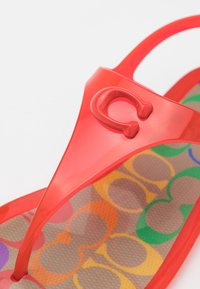 Sandale rouge transparente avec une semelle intérieure colorée à motifs présentant des formes ovales superposées en vert, orange, violet et bleu.