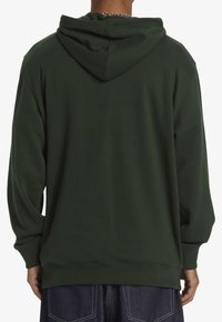 Tmavě zelená mikina s kapucí, žebrovanými manžetami a spodním lemem. Měkký materiál s volným střihem. Minimalistický design, bez viditelných vzorů nebo akcentů.