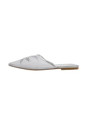 Zapato mule plano puntiagudo plateado con adornos de pedrería en la parte superior y suela marrón.