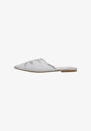 Zapato mule plano puntiagudo plateado con adornos de pedrería en la parte superior y suela marrón.