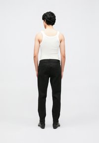 Black trousers and a fitted white tank top. Trousers feature a smooth texture with two back pockets, straight-leg design, and subtle stitching.