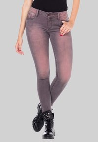 Jean skinny gris avec un léger effet ombragé, comportant cinq poches et une fermeture éclair. Associés à des bottes de combat noires à clous.