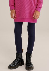 Pink textured oversized sweater, navy leggings, and black patent leather ankle boots with zipper and yellow detail.