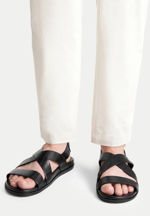 Černé kožené sandály s překříženými pásky, otevřenou špičkou a plochou podrážkou. Nositelná s světlými kalhotami s ohrnutými lemy.