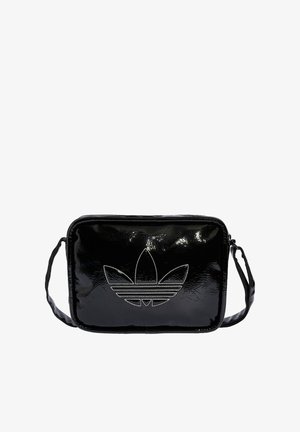 Czarna błyszcząca torebka na ramię z regulowanym paskiem i dużym białym logo Adidas trefoil umieszczonym na środku z przodu.