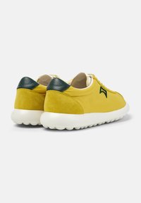 Sneakers gialli con tomaia in pelle liscia, dettagli in suede, particolare verde sul tallone e suola in gomma bianca. Design minimalista con lacci piatti.