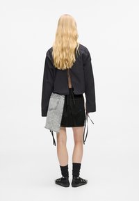 Μαύρο πουκάμισο με μακριά μανίκια και άνοιγμα στην πλάτη, συνδυασμένο με μια μαύρη τζιν φούστα που διαθέτει γκρι τζιν πάνελ και κορδόνια. Οι μαύρες κάλτσες και τα παπούτσια ολοκληρώνουν την εμφάνιση.