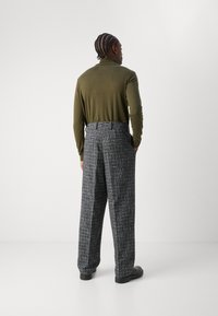 Cămașă verde măsliniu cu mânecă lungă, asociată cu pantaloni cu carouri alb-negru, cu o croială relaxată și buzunare laterale vizibile. Pantofi negri completează ținuta.