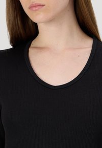 Top preto com nervuras e decote em V, apresentando um tecido texturizado. O design realça o pescoço e a parte superior do torso com uma silhueta ajustada.