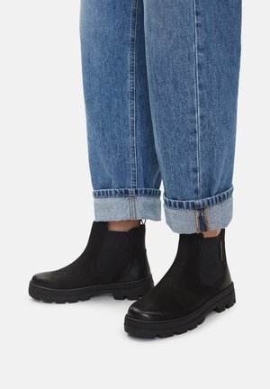 Schwarze Leder-Stiefeletten mit glatter Oberfläche und elastischen Seitenteilen, kombiniert mit hochgekrempelten hellblauen Jeans.
