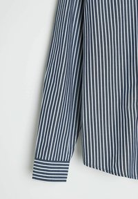 Koszula w pionowe pasy w kolorze granatowym i białym, z długimi rękawami z guzikami przy mankietach, wykonana z lekkiego materiału o gładkiej fakturze.