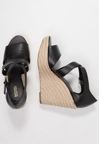 Sandali con zeppa nera in pelle, con cinturini incrociati, tacco avvolto in corda, punta aperta e un dettaglio metallico sul tacco.