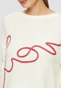 Weißer gestrickter Pullover mit einem strukturierten Muster und einer auffälligen roten Boucle-Stickerei in einem wirbelnden Design auf der Vorderseite.