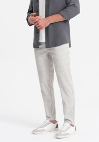 Pantaloni a quadri grigi chiari con una vestibilità rilassata, realizzati in un tessuto testurizzato, abbinati a sneakers bianche con dettagli grigi e lacci.