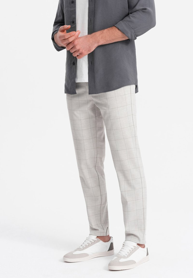 Pantaloni a quadri grigi chiari con una vestibilità rilassata, realizzati in un tessuto testurizzato, abbinati a sneakers bianche con dettagli grigi e lacci.