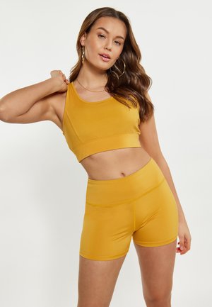 Sárga aktív viselet készlet, amely egy cropped tank topból és magas derekú sortból áll. Az anyag sima, minimalista kialakítással és testhez simuló siluettel rendelkezik.