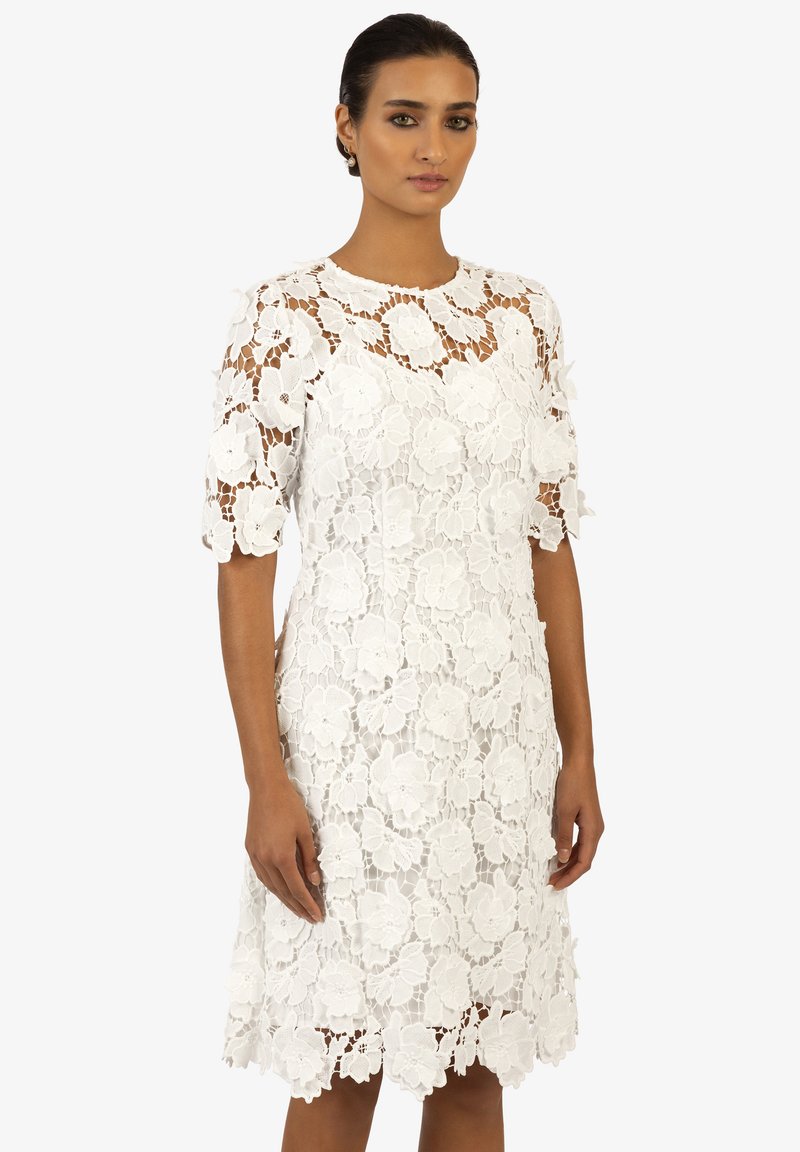 Weißes Spitzenkleid mit Floralprint, knielang, runder Ausschnitt und kurzen Ärmeln. Verfügt über einen gewellten Saum und filigrane Details im gesamten Kleid.