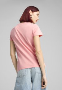 Rožinė medvilninė marškinė su apvalia iškirpte ir trumpomis rankovėmis, derinamos su šviesiai mėlynomis džinsinėmis kelnėmis, pasižyminčiomis laisvu kirpimu ir švelnia tekstūra.