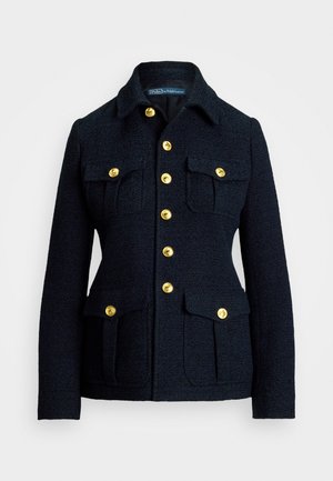 Tumši zili žaketi, kas izgatavots no teksturēta auduma, ar apkakles izgriezumu, zeltītām pogām un četrām priekšējām kabatām ar atloci.