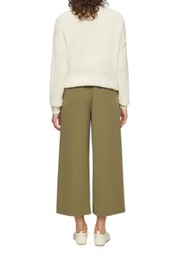 Witte chunky gebreide trui met geribbelde mouwen, gecombineerd met olijfgroene wijde broek. Casual look compleet gemaakt met witte instappers.