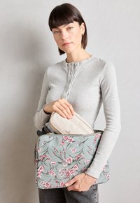 Laptop taske med blomstermønster i lyseblå, prydet med pink blomster. Glat overflade med en guld lynlås. Beige taske delvist synlig indeni.