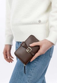 Braunes Lederwallet mit runder Form, Beschlägen in Goldfarbe und einem Frontverschluss mit Riemen. Strukturiert Oberfläche mit glatter Verarbeitung.