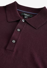 Camisa polo burdeos de tejido texturizado con tapeta de tres botones, cuello acanalado y etiqueta de marca dentro del escote.