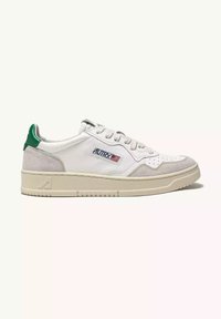 Sneaker bianca con linguetta verde sul tallone, dettagli in pelle scamosciata grigia, punta traforata e suola in gomma testurizzata. Presenta dettagli del logo sul lato.