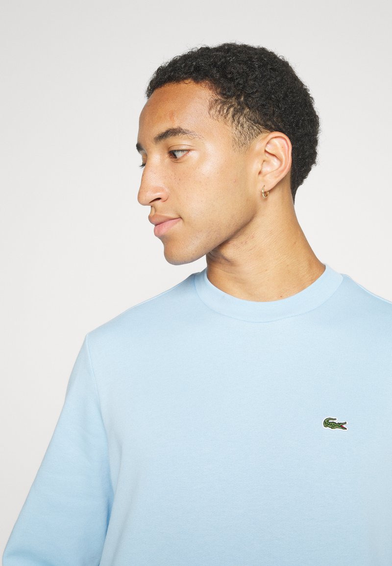 Lichtblauw sweatshirt van zacht katoen, met een ronde halslijn en een klein groen krokodillogo geborduurd op de borst.