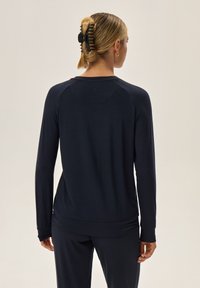 Granatowa koszula z długim rękawem, okrągłym dekoltem, dopasowanymi mankietami i luźnym krojem. Miękka tekstura i prosty design.