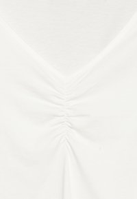 Witte top met een V-hals en geplooide details aan de voorkant. Gemaakt van zachte stof, met een gladde textuur en een eenvoudig ontwerp.