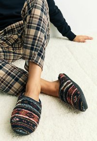 Vlnené pantofle mají vícebarevný pruhovaný vzor v odstínech námořnické modři, burgundy a smetany. Černé gumové podrážky, měkká textura.