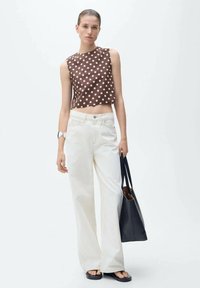 Hnědý top bez rukávů s bílými puntíky, zkombinovaný s bílými volnými džíny; modelka drží černou kabelku a má na sobě ploché sandály.