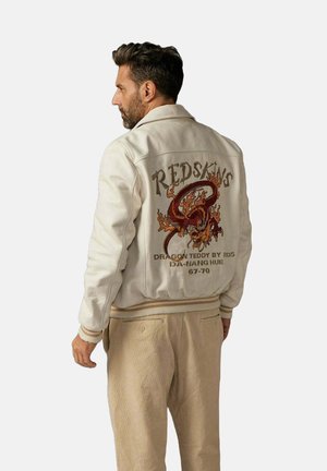 Veste bombardier blanche avec des poignets côtelés. L'arrière présente un design coloré de dragon et le texte "REDSKINS DRAGON TEDDY BY RDS IDN-MANG HUE 67-70."